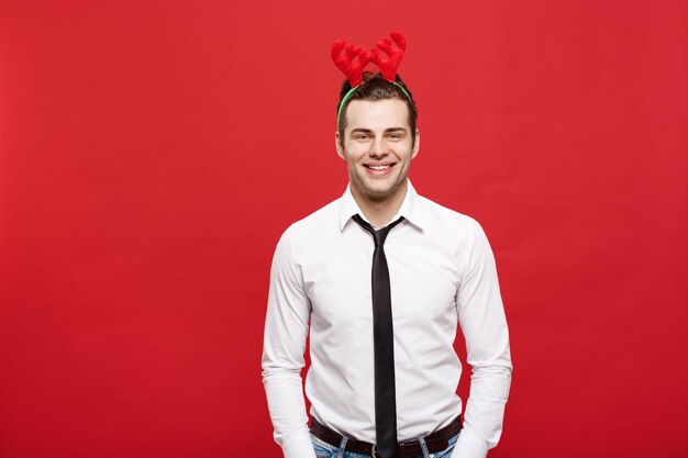 Concepto de Navidad Un hombre de negocios guapo celebra feliz Navidad y feliz año nuevo usa una diadema de reno y sostiene la mano en el bolsillo