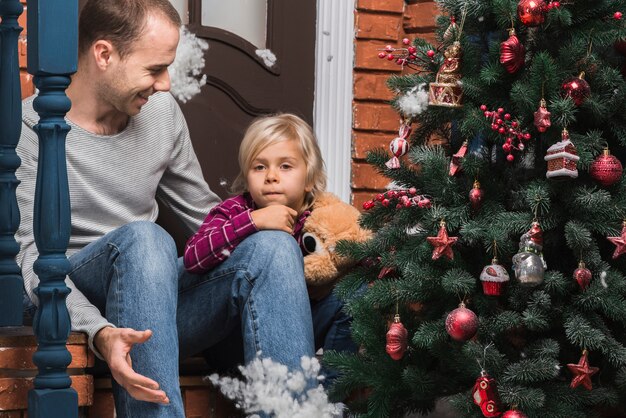 Concepto de navidad con padre e hija fuera con árbol de navidad