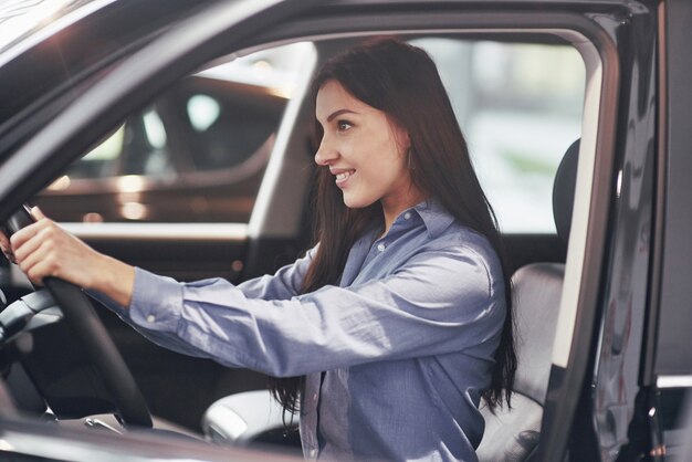 concepto de negocio de automóviles, venta de automóviles, consumo y personas: mujer feliz que toma la llave del automóvil del concesionario en el salón del automóvil