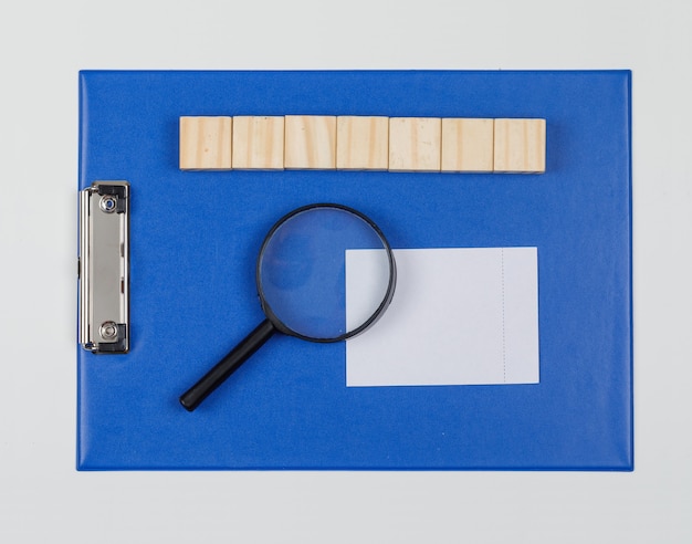 Concepto de negocio con bloques de madera, directorio de papel, lupa, nota adhesiva sobre fondo blanco endecha plana.