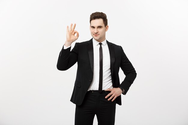 Concepto de negocio: un hombre guapo en traje elegante aislado sobre fondo gris que muestra el signo de ok.