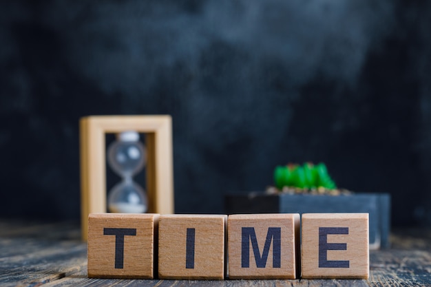 Concepto de negocio con palabra de tiempo en cubos de madera, reloj de arena y planta