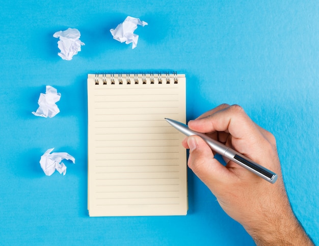 Concepto de negocio con tacos de papel arrugado sobre fondo azul completamente endecha. empresario tomando notas en papel.