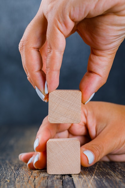 Concepto de negocio en vista lateral de fondo oscuro y madera. manos arreglando el cubo de madera como pila.