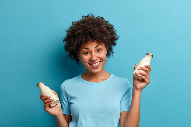 Concepto de nutrición y comida vegana. Alegre mujer de piel oscura con cabello rizado sostiene una botella de leche de almendras frescas