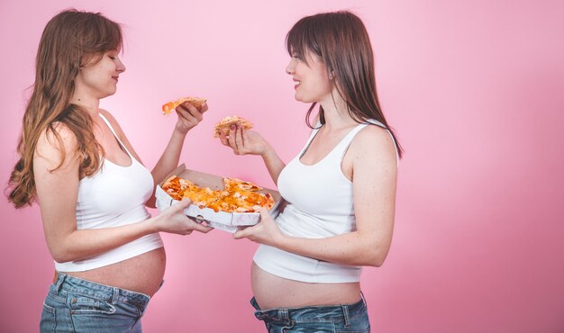 Concepto de nutrición, mujeres embarazadas comiendo pizza en una pared rosa