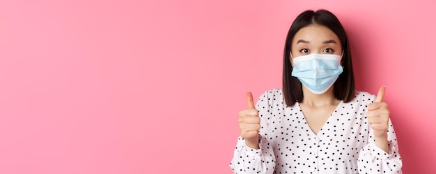 Foto gratuita concepto de pandemia y estilo de vida de covid mujer asiática de apoyo con mascarilla mostrando el pulgar hacia arriba aprobar un