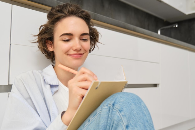 Foto gratuita concepto de pasatiempos y estilo de vida feliz mujer joven se sienta en el piso con bolígrafo y cuaderno wirtes en su di