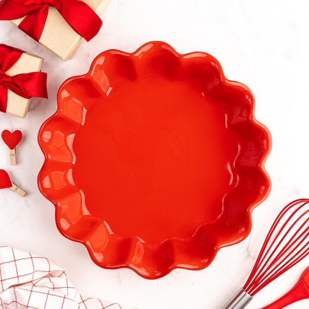 El concepto de pasteles dulces para el día de San Valentín o cumpleaños, fondo culinario con batidor para hornear, cepillo rojo, molde de cerámica y regalos en un fondo blanco, espacio para copiar, vista superior