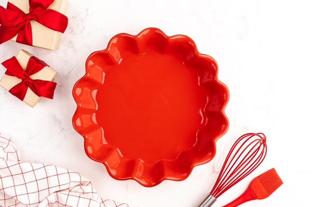 El concepto de pasteles dulces para el día de San Valentín o cumpleaños, fondo culinario con batidor para hornear, cepillo rojo, molde de cerámica y regalos sobre un fondo blanco,
