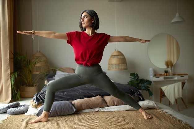 Concepto de personas, actividad, salud y vitalidad. Elegante joven descalza haciendo ejercicio en casa, haciendo vinyasa flow yoga en su dormitorio