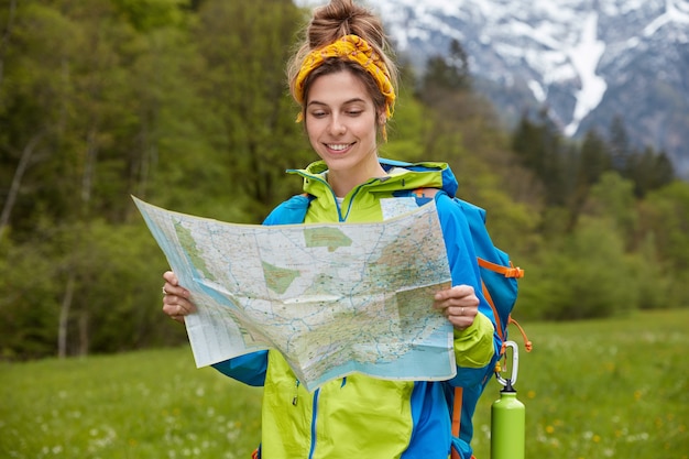 Concepto de personas, aventura y trekking. Feliz turista sostiene mapa de papel, paseos por el valle cerca de las montañas