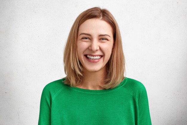 Concepto de personas, belleza y emociones positivas. Atractiva mujer joven sonriente con peinado bobbed, vestida con un suéter casual verde, feliz de recibir el presente