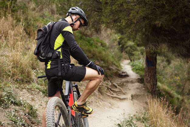 Concepto de personas, deportes, extremos y viajes. Joven jinete del Cáucaso en ropa de ciclismo con unos minutos de descanso durante el entrenamiento al aire libre en la mañana, haciendo ejercicio en su bicicleta de refuerzo