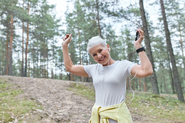 Foto gratuita concepto de personas, edad, diversión y estilo de vida activo. feliz mujer de mediana edad escuchando la lista de reproducción en ejecución con teléfono inteligente.