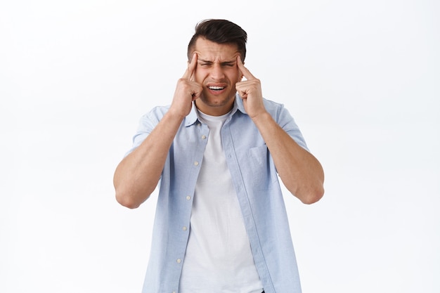 Foto gratuita concepto de personas y emociones de salud. retrato de hombre adulto guapo entrecerrando los ojos y haciendo muecas como no puedo leer el letrero sin gafas, tiene mala vista, visita al óptico para revisar los ojos, pared blanca