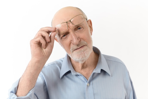 Concepto de personas, envejecimiento, gafas, visión y óptica. Imagen horizontal de un anciano hipermétrope con barba blanca quitándose las gafas y frunciendo el ceño para ver claramente lo que está frente a él