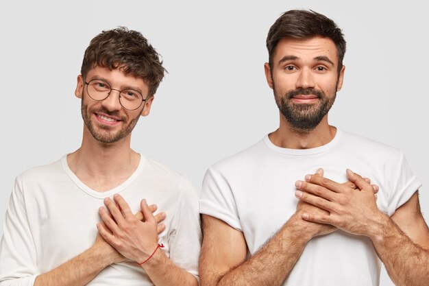 Concepto de personas y gratitud. Estudiantes agradecidos de dos hombres felices de recibir buenas calificaciones en el examen, tienen barba y bigote, vestidos con una camiseta blanca informal