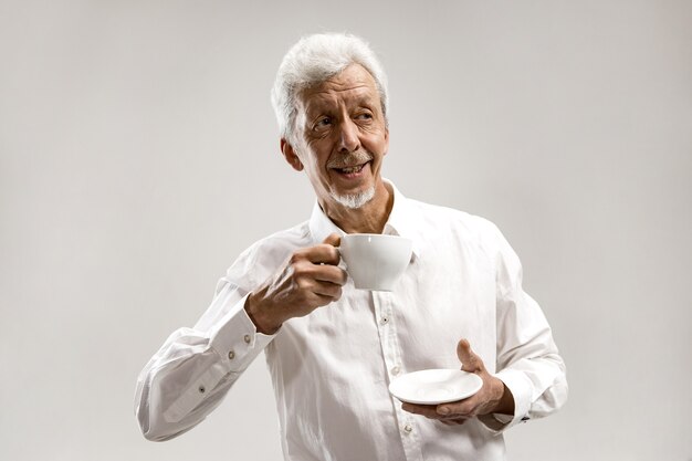 Concepto de personas - hombre mayor feliz con taza de té en el estudio. Concepto de emociones humanas