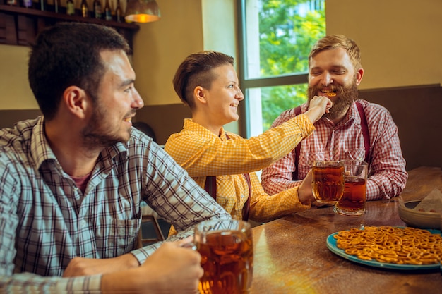 Concepto de personas, ocio, amistad y comunicación: amigos felices bebiendo cerveza, hablando y tintineando vasos en el bar o pub