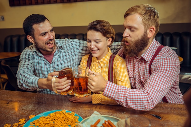 Concepto de personas, ocio, amistad y comunicación: amigos felices bebiendo cerveza, hablando y tintineando vasos en el bar o pub