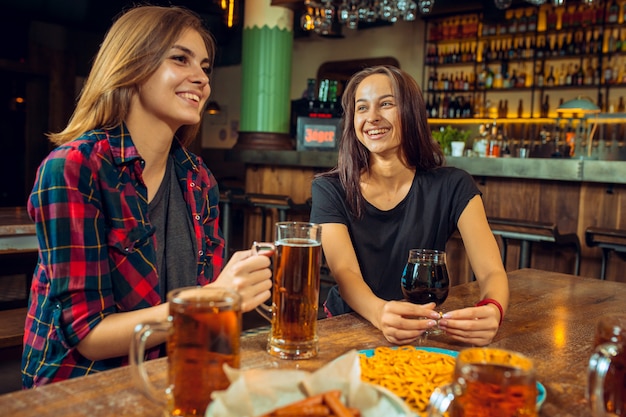 Concepto de personas, ocio, amistad y comunicación: amigos felices bebiendo cerveza, hablando y tintineando vasos en el bar o pub