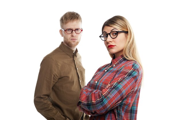 Concepto de personas, relaciones, trabajo, carrera, cooperación y trabajo en equipo. Retrato de compañeros de trabajo joven sin afeitar y mujer rubia en gafas posando con los brazos cruzados, con miradas serias