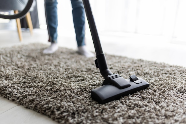 Concepto de personas, tareas domésticas y servicio de limpieza - cerca de mujer con piernas aspiradora limpieza de alfombras en casa