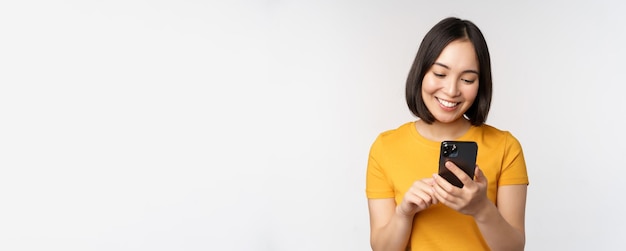 Concepto de personas y tecnología niña asiática sonriente usando mensajes de texto de teléfonos inteligentes en un teléfono móvil de pie