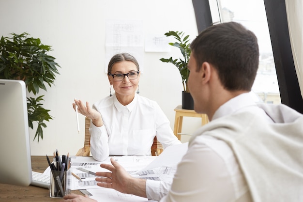 Concepto de personas, trabajo en equipo, éxito, tecnología y ocupación. Ingeniera senior experimentada que trabaja en equipo junto con un joven hábil, intercambio de ideas, con una agradable discusión animada