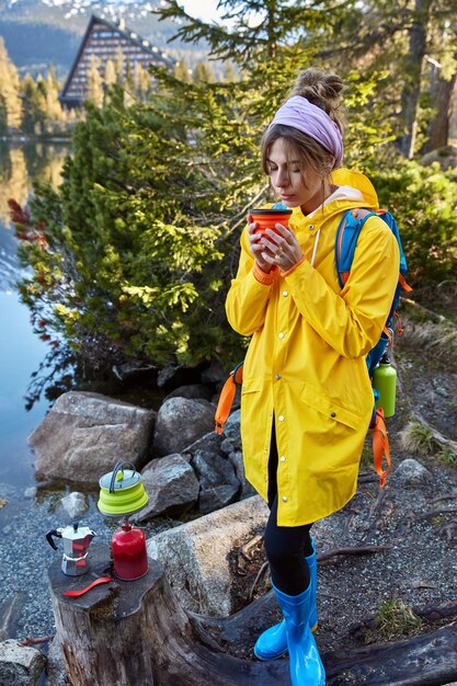 Concepto de personas, vacaciones y camping. Mujer europea huele café aromático, sostiene una taza desechable
