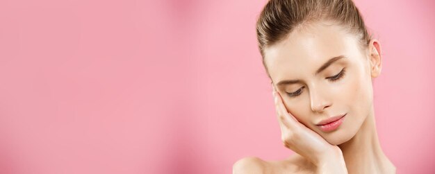 Concepto de piel de belleza Hermosa mujer caucásica joven con piel limpia y fresca mirar hacia otro lado con fondo de estudio rosa Cuidado de la cara de belleza de niña Tratamiento facial Cosmetología belleza y spa