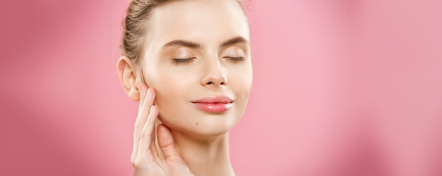 Concepto de piel de belleza Hermosa mujer caucásica joven con piel limpia y fresca mirar hacia otro lado con fondo de estudio rosa Cuidado de la cara de belleza de niña Tratamiento facial Cosmetología belleza y spa