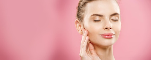 Concepto de piel de belleza Hermosa mujer caucásica joven con piel limpia y fresca mirar hacia otro lado con fondo de estudio rosa Cuidado de la cara de belleza de niña Tratamiento facial Cosmetología belleza y spa