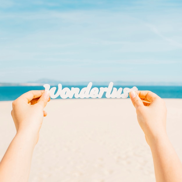 Concepto de playa con manos sujetando letras que ponen wonderlust