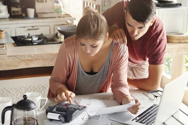 Concepto de presupuesto y finanzas familiares. Joven seria esposa y esposo haciendo cuentas juntos en casa