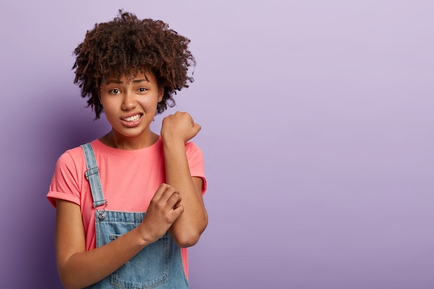 Concepto de problema de piel. Mujer afro disgustada rasca el brazo con picazón