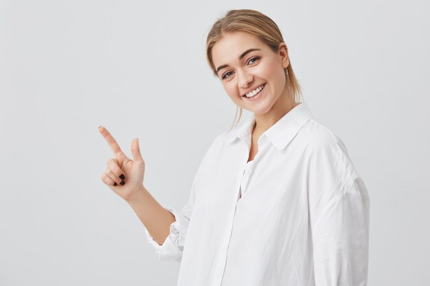 Concepto de publicidad. Feliz mujer joven con cabello rubio con ropa casual, de pie con espacio de copia para su información o contenido promocional