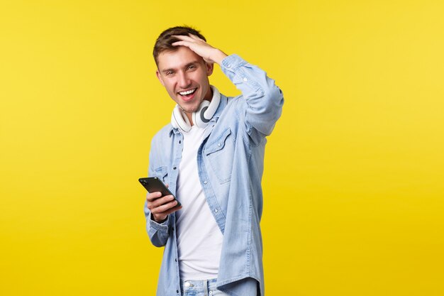 Concepto de publicidad de ocio, tecnología y aplicaciones. Chico moderno y elegante alegre en ropa casual, tocando el corte de pelo, actuando con calma y confianza, enviando mensajes con el teléfono inteligente, usando la aplicación.