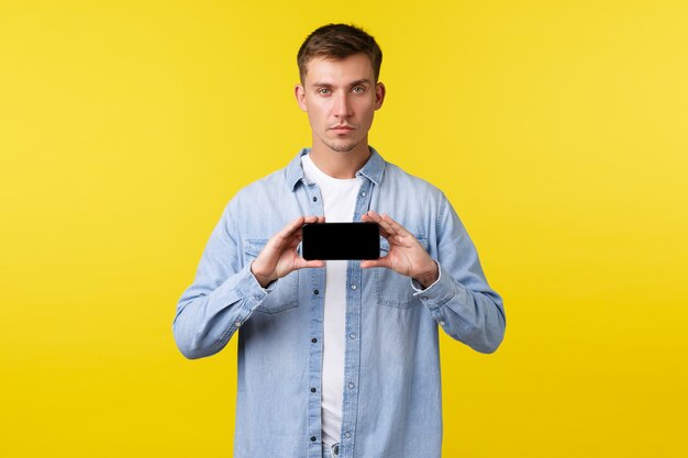 Concepto de publicidad de ocio, tecnología y aplicaciones. Hombre rubio de aspecto serio que intenta llamar la atención a información importante, mostrando un banner o una aplicación en la pantalla del teléfono inteligente.