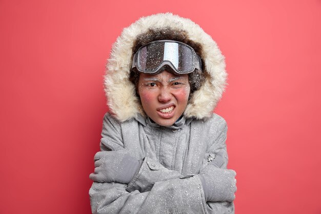 Concepto de recreación y ocio activo. Mujer insatisfecha aprieta los dientes y se abraza a sí misma, ya que siente escalofríos durante el helado enero viste ropa abrigada para el clima frío durante el invierno