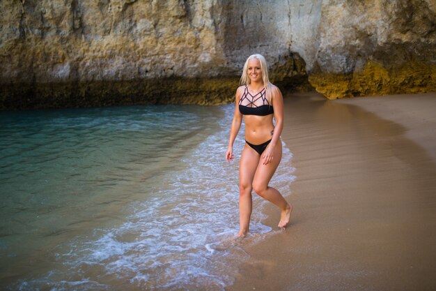 Concepto de recreación de verano. Hermosa joven sexy con cuerpo delgado entrenado en forma con bikini traje de baño negro camina en una playa junto al mar