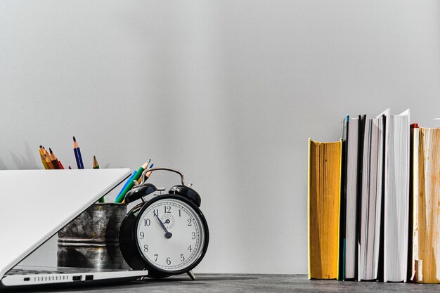 Concepto de regreso a la escuela o idea del día del maestro Bolígrafos, lápices, libros, un despertador y una computadora portátil en la mesa contra el fondo de un tablero gris Regreso a la escuela con espacio para copiar