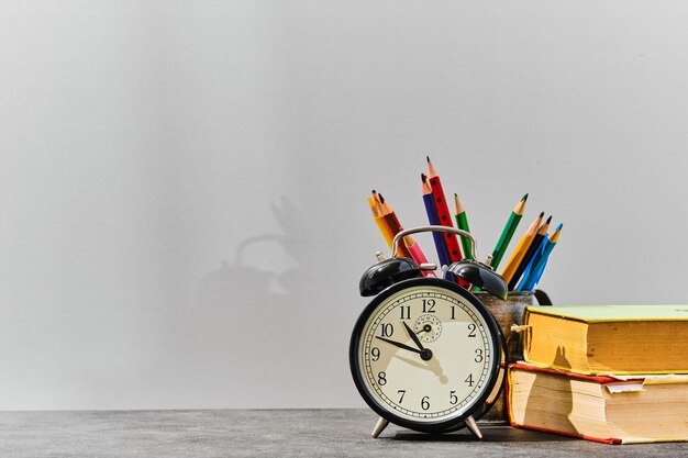 Concepto de regreso a la escuela o idea del día del maestro Bolígrafos, lápices, libros, un despertador en la mesa contra el fondo de un tablero gris con espacio para copiar