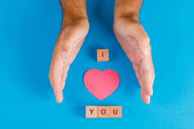 Concepto de relación con cubos de madera en la mesa azul plana lay. manos protegiendo papel cortado corazón.