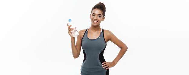 Concepto de salud y fitness hermosa chica afroamericana en ropa deportiva sosteniendo una botella de agua de plástico después del entrenamiento aislado sobre fondo blanco de estudio