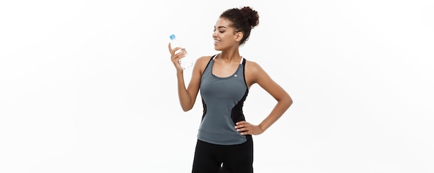 Concepto de salud y fitness hermosa chica afroamericana en ropa deportiva sosteniendo una botella de agua de plástico después del entrenamiento aislado sobre fondo blanco de estudio