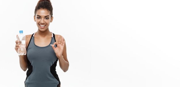 Concepto de salud y fitness hermosa chica afroamericana en ropa deportiva sosteniendo una botella de agua de plástico después del entrenamiento aislado sobre fondo blanco de estudio