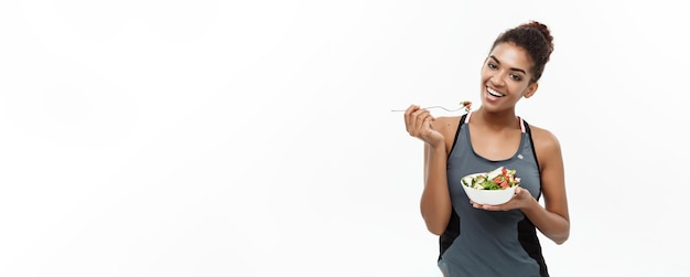 Concepto de salud y fitness Hermosa dama africana americana en ropa de fitness en dieta comiendo ensalada fresca Aislada sobre fondo blanco