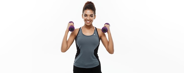 Concepto de salud y fitness Hermosa dama africana americana en ropa de fitness entrenamiento con mancuernas aislado sobre fondo blanco.